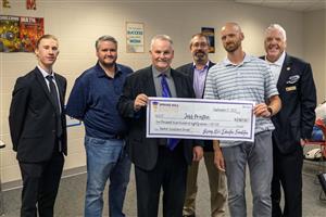 Jeff Preston holding a novelty check & SHEF Board smiling for the Teacher Excellence Grant presentation at SHMS